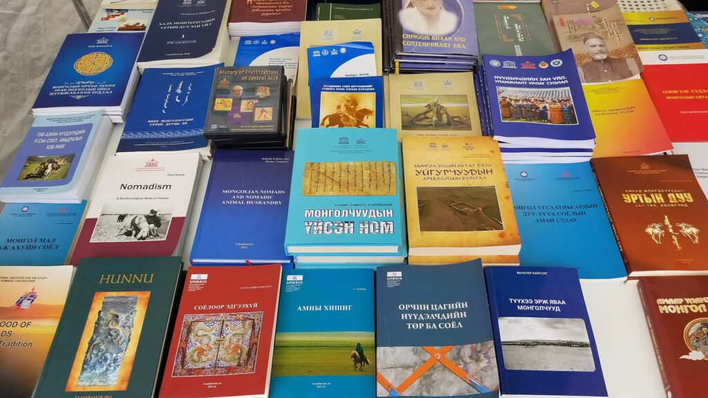 Gestapelte B&uuml;cher mit abgegriffenen R&uuml;cken liegen auf einem Tisch neben einer Lampe