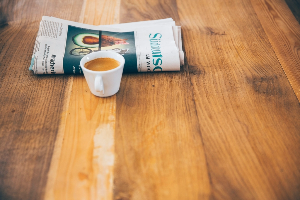 Mehrere gefaltete Zeitungen liegen &uuml;bereinander auf einem Tisch neben einer Tasse