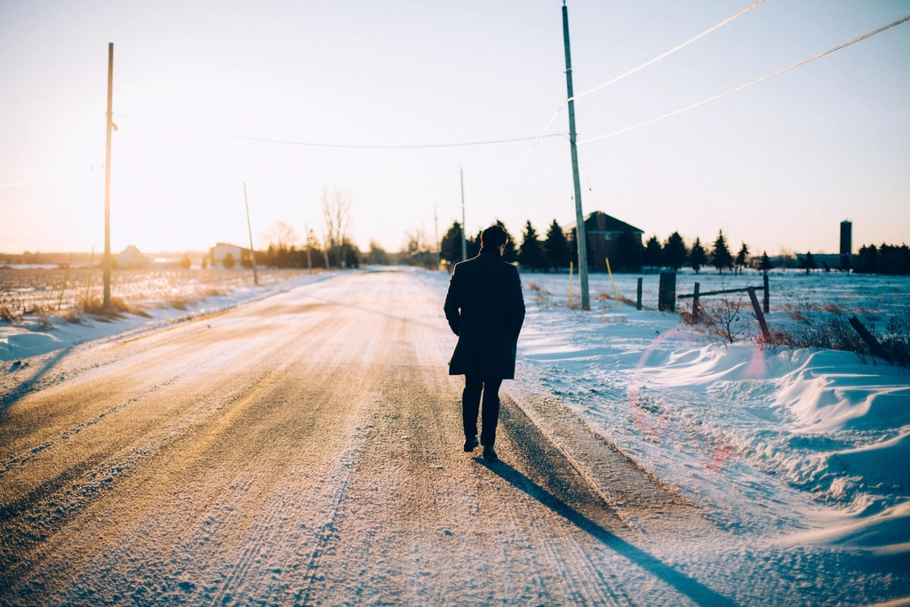 Eine Person geht in warmer Kleidung an einem hellen Vormittag über einen Feldweg