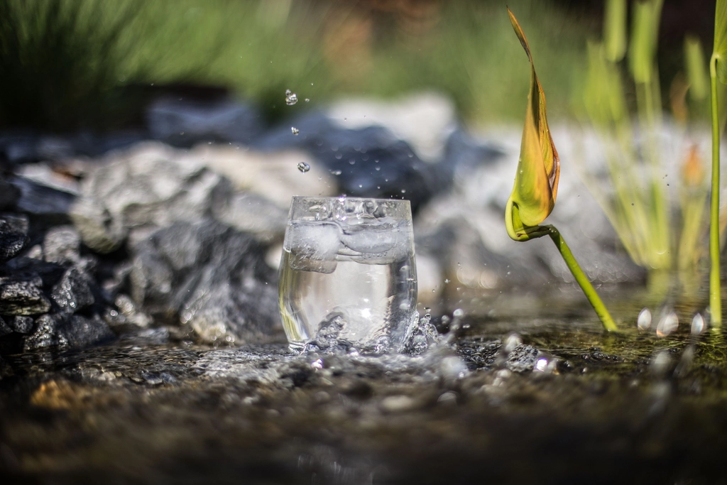 Ein gefülltes Wasserglas steht auf einem schmalen Tisch am Fenster