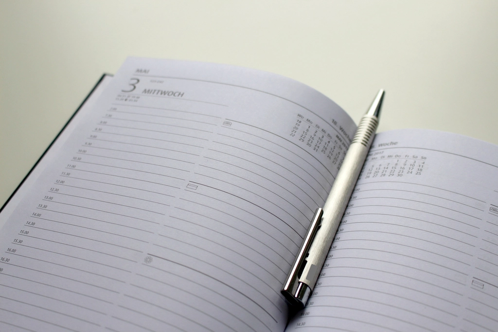 Ein aufgeschlagener Wandkalender mit handschriftlichen Notizen und einem daneben liegenden Stift